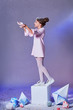 Beautiful young little child in elegance pink dress for party standing on a cube, catches snow by hand. Holidays, christmas, new year, x-mas, Fashion concept. Studio, purple background.