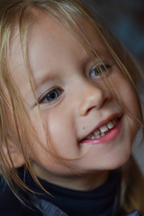 Portrait of a joyful romantic little girl with big blue eyes and an open smile from Eastern Europe, close-up, dark background