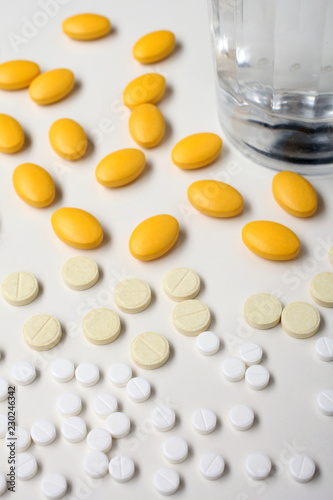 Foto A pile of white and yellow pills and bottom of glass on a white background