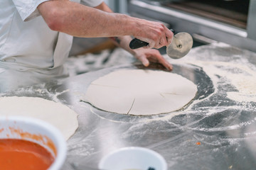 Cooking Italian national food with chef and ingredients for pizza. Dough in chef hand on a dark black background of wood. Baking bread, pizza, pasta. Recipe from chef cooks pizza.