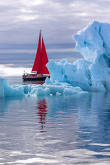 Wall Mural - beautiful red sailboat in the arctic next to a massive iceberg showing the scale. ilulissat, disko b
