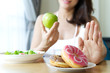 Woman rejecting junk food or unhealthy food such as donuts and choosing healthy food such as a green apple and salad for having a good health. Dieting and good health concept.