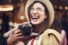 Cheerful Happy Young Long Haired Lady Holing Adorable Puppy And Closing Her Eyes While Laughing