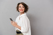 © Drobot Dean - Photo of attractive woman 20s smiling and holding mobile phone, isolated over gray background