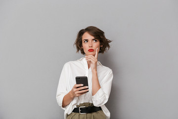 Poster - Photo of charming woman 20s smiling and holding mobile phone, isolated over gray background