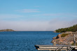 Looking towards a Baltic inlet in Kökar, a municipality of the Åland Islands, Finland, under a soft cloudy blue sky with a dark haze rolling in, during mid-morning near midsummer.