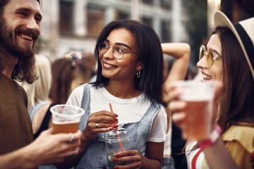 Wall Mural - Portrait of young beautiful lady with cocktail looking at bearded man and holding cocktail. Woman in hat chatting with gentleman while he holding beer