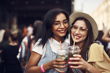 Wall Mural - Cheers. Portrait of young ladies in glasses holding drinks and looking at camera with happy smiles