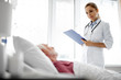 © Yakobchuk Olena - I am checking your condition. Portrait of young lady in white lab coat holding clipboard and looking at patient
