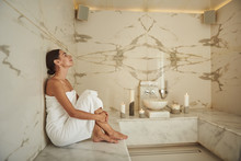 Calm Peaceful Young Woman Wearing White Towel And Sitting Next To The Wall Of Comfortable Hammam
