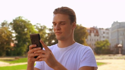 Poster - young caucasian man walking using smartphone. handsome businessman texting message on mobile outdoors