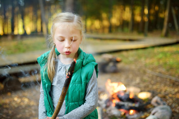 Wall Mural - cute little girl roasting marshmallows on stick at bonfire. child having fun at camp fire. camping w