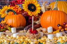 Popcorn Peanuts Marshmallows And Red Candy Apple On Blue Table With Background Of Fall Flowers Berries Nuts Autumn Leaves Yellow Sunflowers And Orange Pumpkins On Burlap