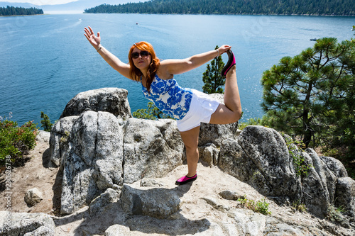Fotografie, Obraz Red head hair ginger woman does a yoga mediation pose on a rock on Fannette Isla