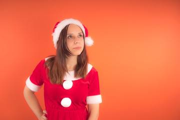 Wall Mural - Portrait of a young girl dressed as Santa Claus on orange background. Happy New year and merry Christmas!