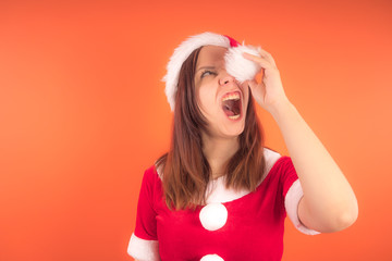 Wall Mural - Portrait of a young girl dressed as Santa Claus on orange background. Happy New year and merry Christmas!