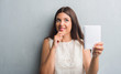 © Krakenimages.com - Young brunette woman over grunge grey wall showing notebook serious face thinking about question, very confused idea