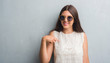 © Krakenimages.com - Young brunette woman over grunge grey wall wearing retro sunglasses with surprise face pointing finger to himself