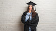 © Krakenimages.com - Young brunette woman standing over white brick wall wearing graduate uniform serious face thinking about question, very confused idea
