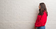 © Krakenimages.com - Young brunette woman standing over white brick wall looking to side, relax profile pose with natural face with confident smile.