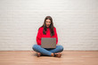 © Krakenimages.com - Young brunette woman sitting on the floor over white brick wall using laptop scared in shock with a surprise face, afraid and excited with fear expression