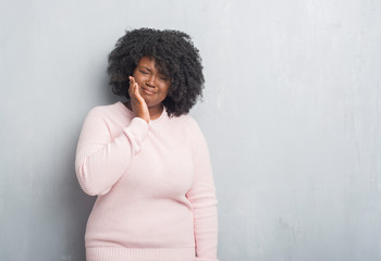 Poster - Young african american plus size woman over grey grunge wall wearing winter sweater touching mouth with hand with painful expression because of toothache or dental illness on teeth. Dentist concept.