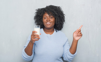 Sticker - Young african american woman over grey grunge wall drinking a glass of milk very happy pointing with hand and finger to the side