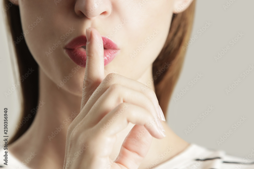 Finger on lips - silent gesture, Woman holding her finger to her lips in a gesture for silence. - obrazy, fototapety, plakaty 