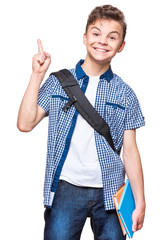 Wall Mural - Portrait of cheerful teen boy with good idea. Cute schoolboy with school bag and books pointing up, isolated on white background. 