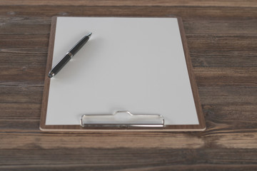 Clipboard with white sheet and pen on wood background. Top view.Vintage style.