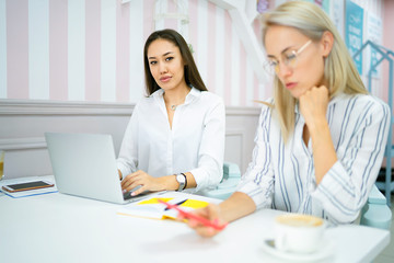 Skilled group of journalists creating publication discussing details using laptop computer and wifi connection while sitting in cafe. Two girls talk sitting at the desk at the cafe.