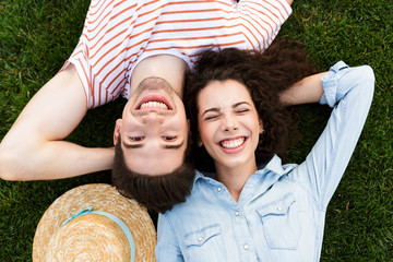 Poster - Image from top of joyous couple man and woman 20s, lying alongside opposite heads on green grass in park