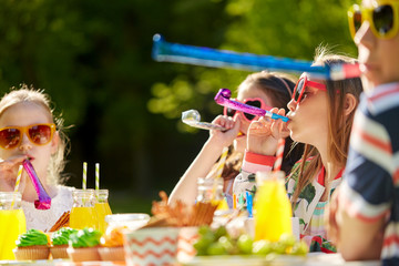 Poster - birthday, childhood and celebration concept - close up of happy kids blowing party horns and having fun in summer