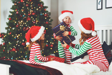 Wall Mural - happy family mother and children in pajamas opening gifts on christmas morning near   tree