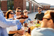 © Syda Productions - leisure and people concept - happy party host offering meat to his friends at barbecue party on rooftop in summer