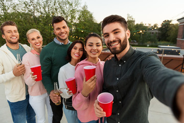 Canvas Print - leisure and people concept - happy friends with drinks taking selfie at rooftop party in summer