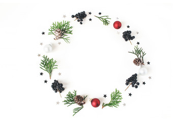 Wall Mural - Christmas circle floral composition. Wreath of green cypress branches, larch cones, Christmas glass balls, baubles, silver confetti stars and black privet, berries. White table background. Flatlay