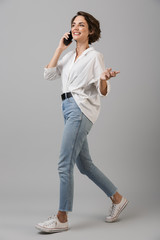 Poster - Emotional young business woman posing isolated over grey wall background talking by mobile phone.