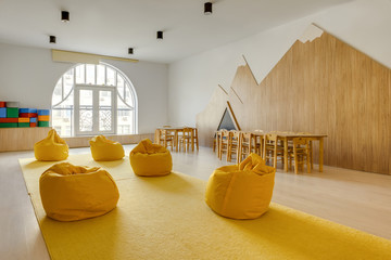 yellow bean bag chairs and wooden tables in kindergarten playing room