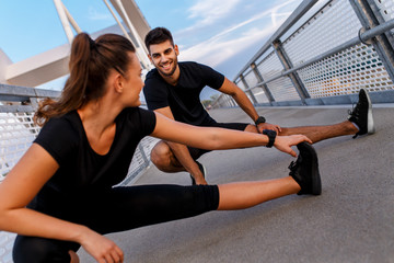 Wall Mural - Young couple doing morning workout outdoors. Young man and woman stretching they muscle before running on bridge.