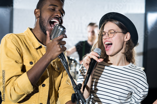 Fotografia Waist up portrait of two young people enjoying singing with microphones during b