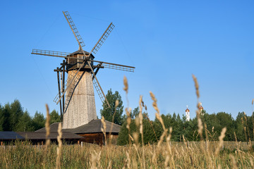 Wooden windmill with ears of wheat growing in the field on the foreground