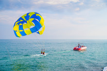 Parachute Water Fun. Flight By Parachute Behind The Boat On The Black Sea, In The Resort. Beautiful Water And Blue-yellow Parachute.