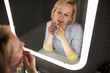 © pressmaster - Young attractive blond Caucasian woman popping pimple on her chin while looking at herself in bathroom mirror