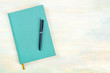 A photo of a teal blue journal with a pen, an elegant diary, notebook or planner, shot from above with copy space
