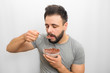 © estradaanton - Nice brunette stands and eats chocolate round chips with milk. He is going to put spoon with it in mouth. Guy is sleepy. He looks down. Isolated on white background.
