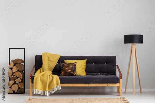 Fotografia Log of wood next to comfortable sofa with yellow blanket and pillows, stylish wo
