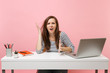 © ViDi Studio - Young exhausted irritated woman in perplexity spreading hands sit, work at white desk with contemporary pc laptop isolated on pastel pink background. Achievement business career concept. Copy space.