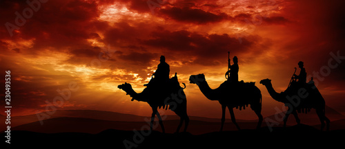 Cuadros en Lienzo Three kings - traveling in the desert against the background of red clouds risin