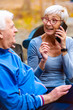 © lordn - Smiling senior active couple sitting on the bench looking at smartphone